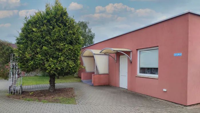 Wejście do biura Chemix. Duże zielone drzewo stojące przed czerwonym budynkiem.