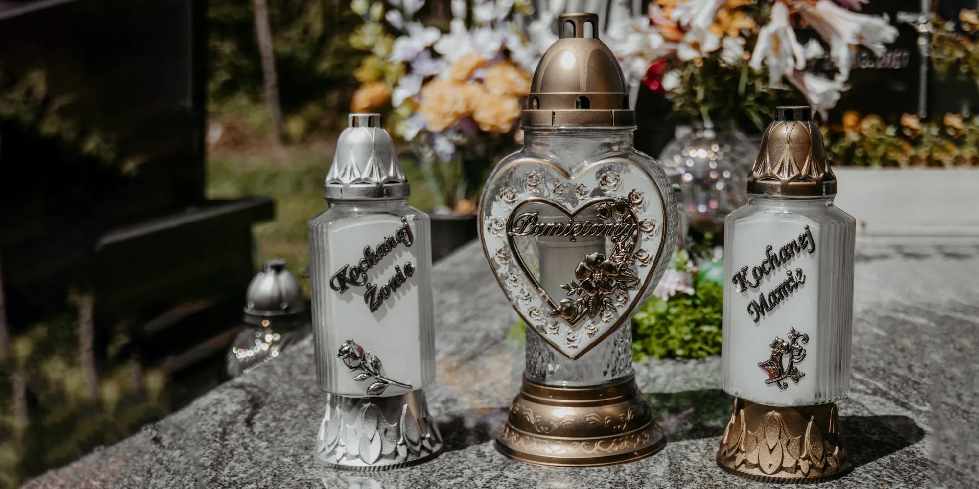 Znicze na grobie. Kwiaty w tle